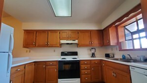 A kitchen with wooden cabinets, a stove, a refrigerator, and a window. - Comfy Newly Furnished Home (Warrensburg)
