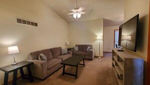 A living room with a sofa, two side tables, a coffee table, a TV, and a ceiling fan. - Comfy Newly Furnished Home (Warrensburg)