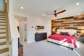 A bedroom with a wooden wall panel, a ceiling fan, a bed with red bedding, a dresser, and a nightstand. - Durham Vacation Rental w/ Community Pools! (Durham)