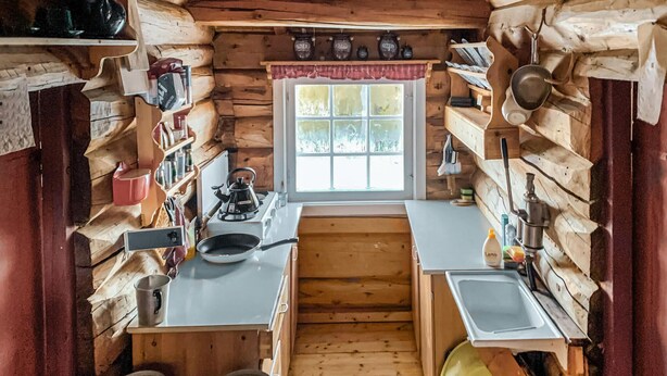 A compact kitchen with wooden walls, a window, and basic amenities like a kettle, pots, and a sink. - Cozy home in Vinstra with kitchen (Vinstra)