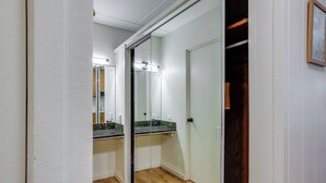 Un pasillo estrecho con suelo de madera, un vidrio y un espejo que refleja una cocina con encimera y armarios.