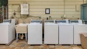 Un cuarto de lavandería con cuatro lavadoras de carga frontal, un lavabo y un panel eléctrico en la pared.