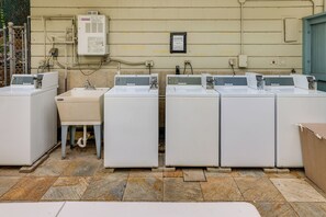 A laundry facility with four front-loading washing machines, a sink, and an electrical panel on the wall.