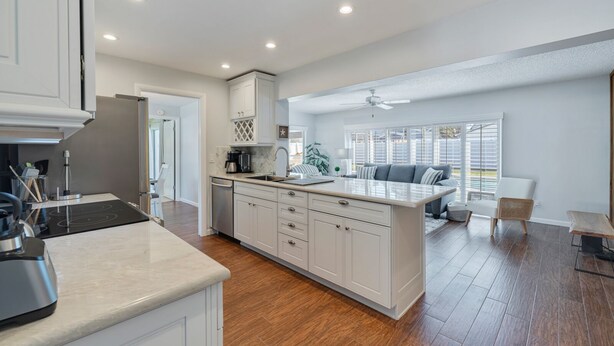 A modern kitchen with white cabinetry, a central island, and a dining area with a gray sofa and wicker chairs. - My Happy Place – Heated Pool, Dual Living Rooms, Screened Lanai & Nearby Indian Rocks Beach (Seminole)