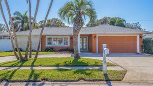 A single-story house with a garage, a front yard with palm trees, and a mailbox. - My Happy Place – Heated Pool, Dual Living Rooms, Screened Lanai & Nearby Indian Rocks Beach (Seminole)