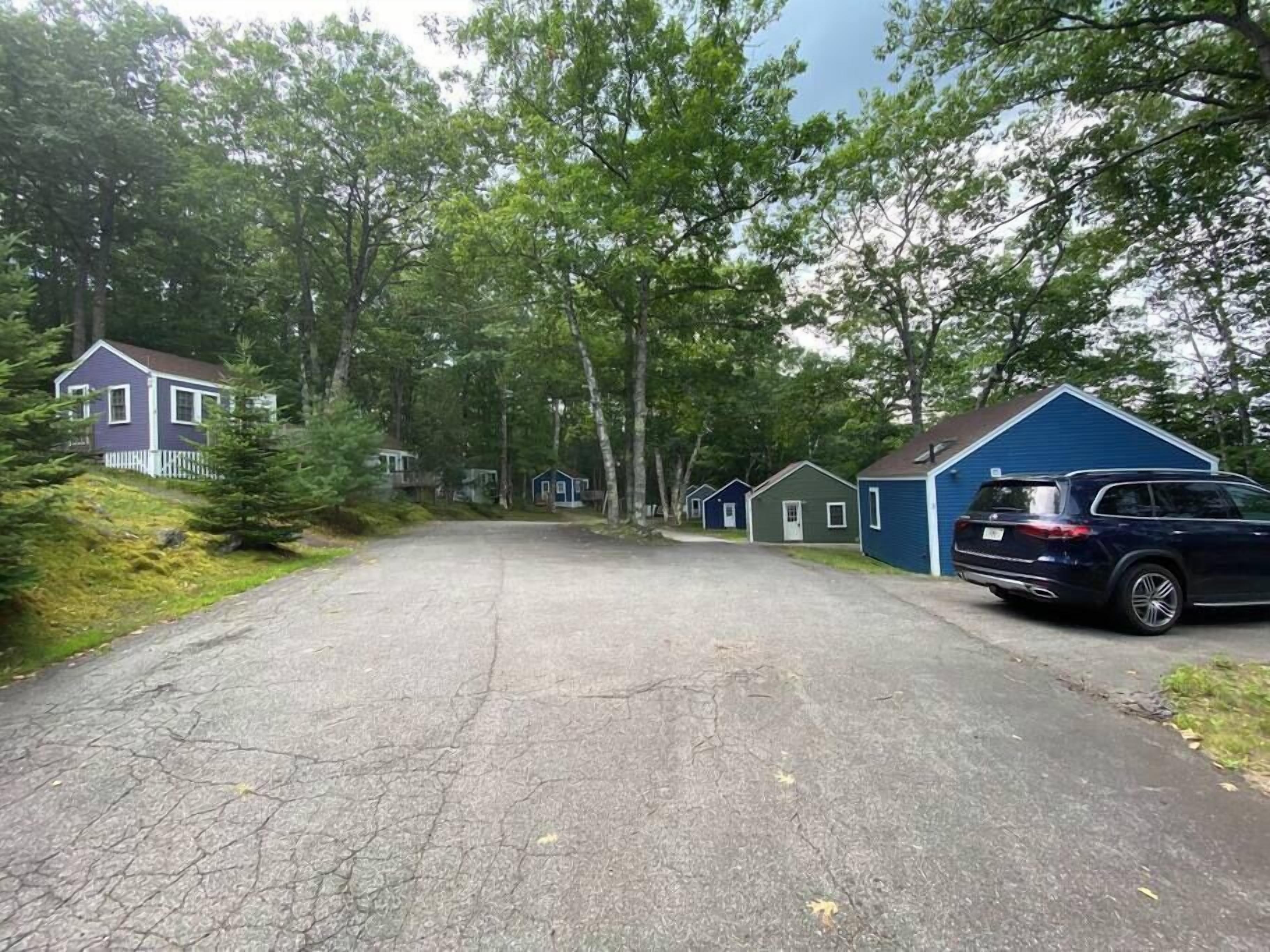 A row of small, single-story cabins with a paved driveway leading to them, surrounded by trees.