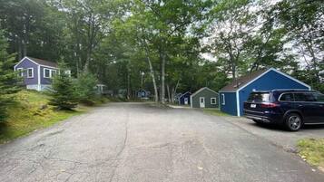 A row of small, single-story cabins with a paved driveway leading to them, surrounded by trees.