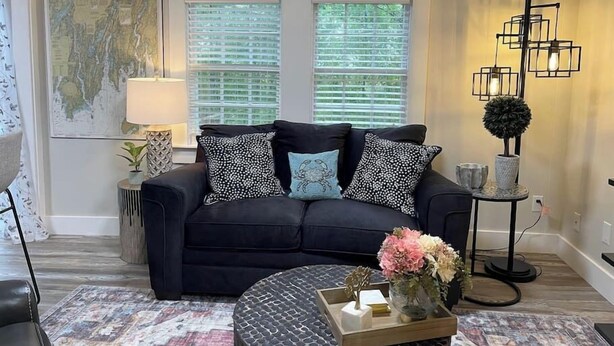 A living room with a dark sofa, patterned cushions, a round coffee table with a tray, a lamp, and a map on the wall. - Spacious 1 Bedroom Cottage Close to Everything 5 (Edgecomb)