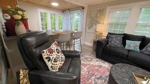 A living room with a black leather sofa, a patterned rug, and a dining area with a table and chairs.
