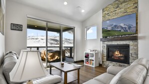 Un salon moderne avec une cheminée, un canapé, une table et une vue sur un paysage enneigé, visible à travers de grandes portes coulissantes.