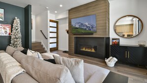 Un salon moderne avec une cheminée, un grand téléviseur à écran plat, un sapin de Noël et un escalier menant à un autre niveau.