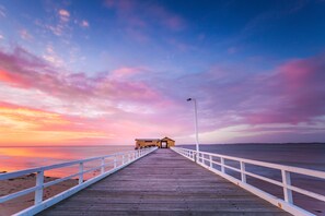 Un muelle de madera que lleva a un edificio con barandilla blanca, con vista a una masa de agua tranquila.