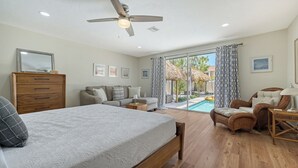 A bedroom with a bed, a dresser, a sofa, a chair, and a view of a swimming pool.
