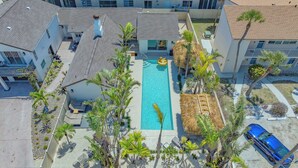 A rooftop pool surrounded by palm trees and a blue car, with buildings in the background.