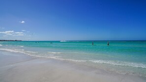 A beach with clear turquoise water, a sandy shore, and a few people in the distance. - 3 bedroom, 4 bath, private pool home, steps to Crescent beach, sleeps 8 (Siesta Key)