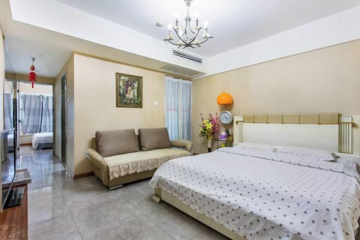 Une chambre d’hôtel avec un lit, un canapé, un lustre, une horloge et une fenêtre avec des rideaux.