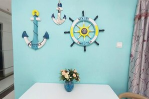 A room with a light blue wall, a white table, and a vase with flowers. There are two wall decorations: one is an anchor with the word 'WELCOME' and the other is a ship's wheel with the word 'WELCOME'. - Jufuyuan Apartment (Shenzhen)