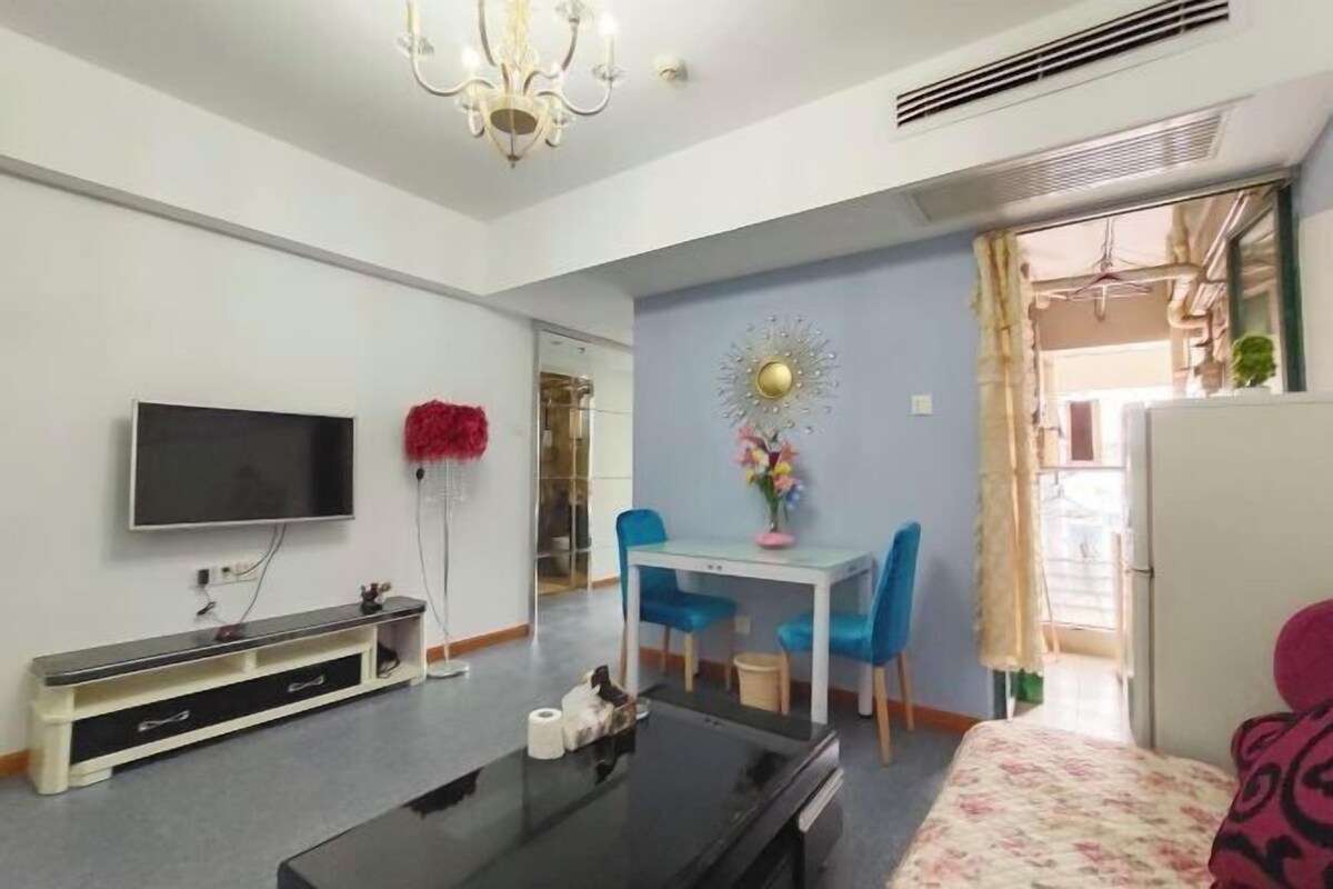Una sala de estar moderna con un televisor de pantalla plana, una mesa de centro, un sofá, una mesa de comedor con sillas azules y un espejo decorativo.