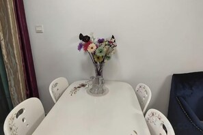 Ein Esstisch mit einer klaren Glasvase und Blumen, umgeben von weißen Stühlen mit Blumenmuster.