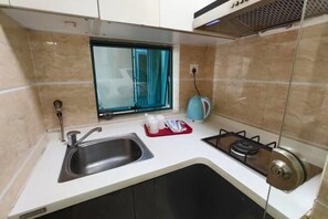 Una cocina compacta con un lavamanos, una estufa a gas y una ventana con cortinas.