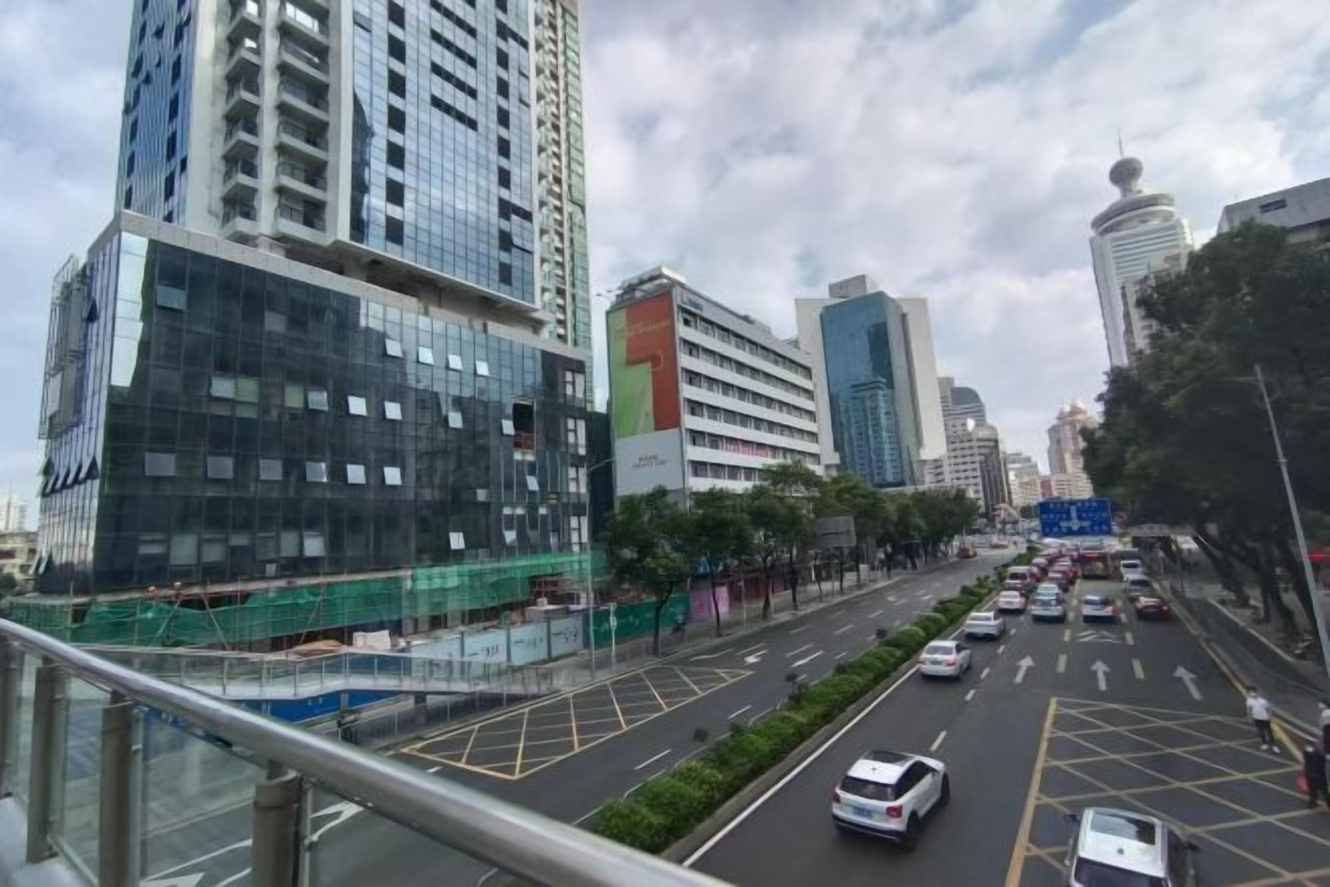 A city street with tall buildings, a pedestrian walkway, and vehicles.