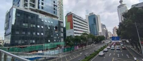 Rua urbana com edifícios altos, calçada para pedestres e veículos.
