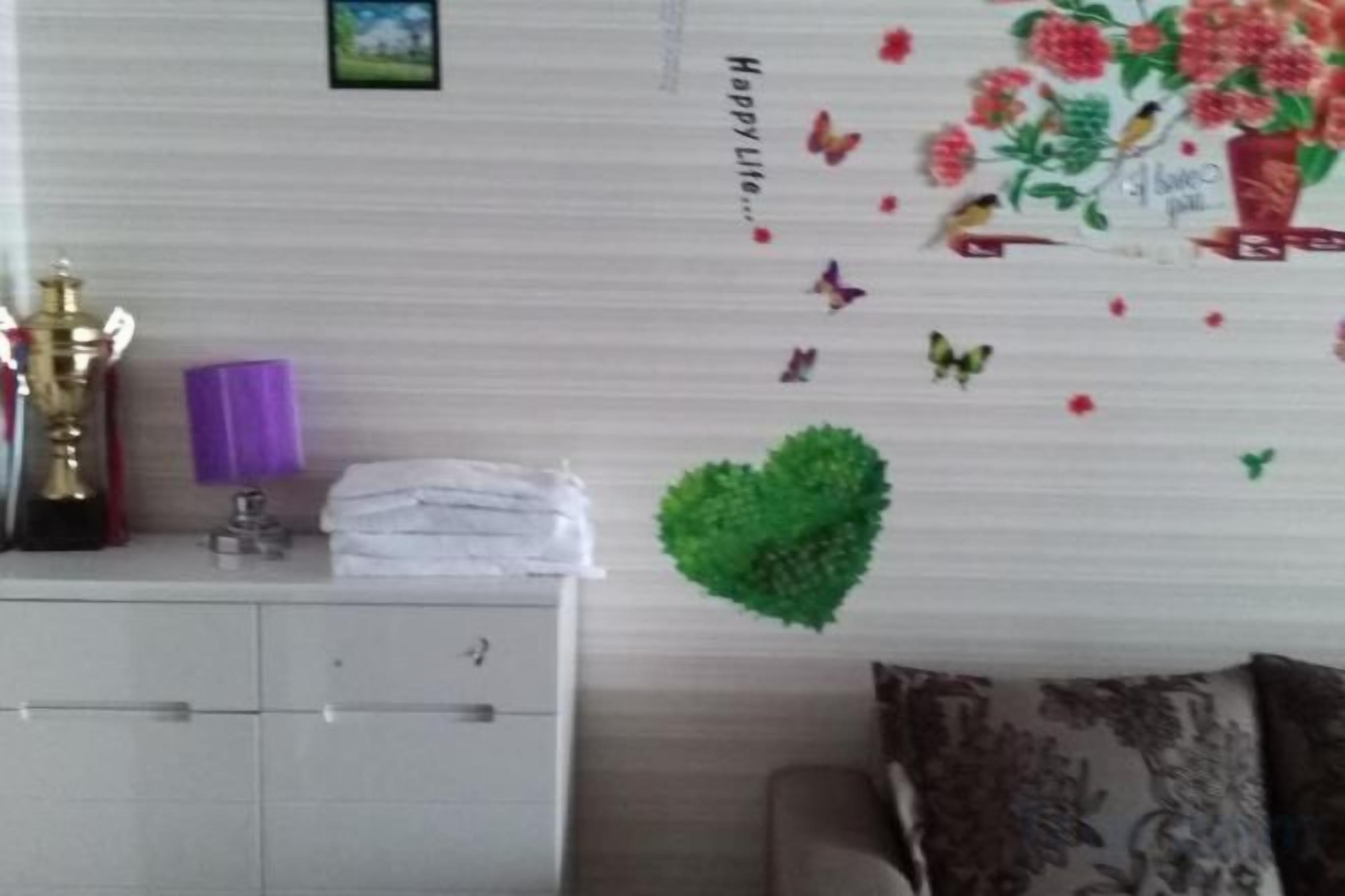 A room with a white cabinet, a decorative wall with a heart and butterflies, and a couch with a patterned cushion.