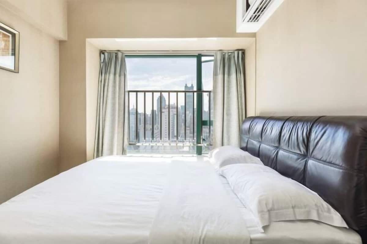 Une chambre d’hôtel avec un lit, une vue sur le paysage urbain par la fenêtre et une bouche d’aération au plafond.