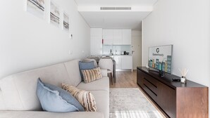 Una sala moderna con un sofá, un televisor y una cocina al fondo.