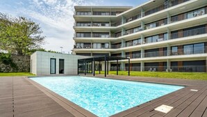 Un edificio moderno de varios pisos con piscina, zona de estar al aire libre y patio cubierto.