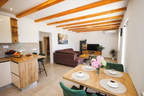 Eine moderne Küche mit Holzbalken, einem Essbereich mit Tisch für zwei Personen und einem Wohnbereich mit Sofa.