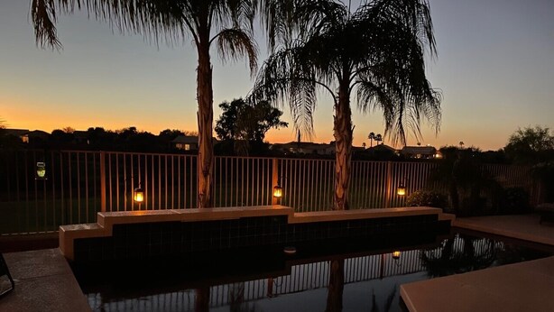 A swimming pool with a wooden deck and railings, surrounded by palm trees and a fence. - Private Pool on the Golf Course in Surprise (Surprise)