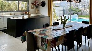 Une cuisine moderne avec un coin repas, comprenant un grand îlot central, des luminaires suspendus et une vue sur une piscine.