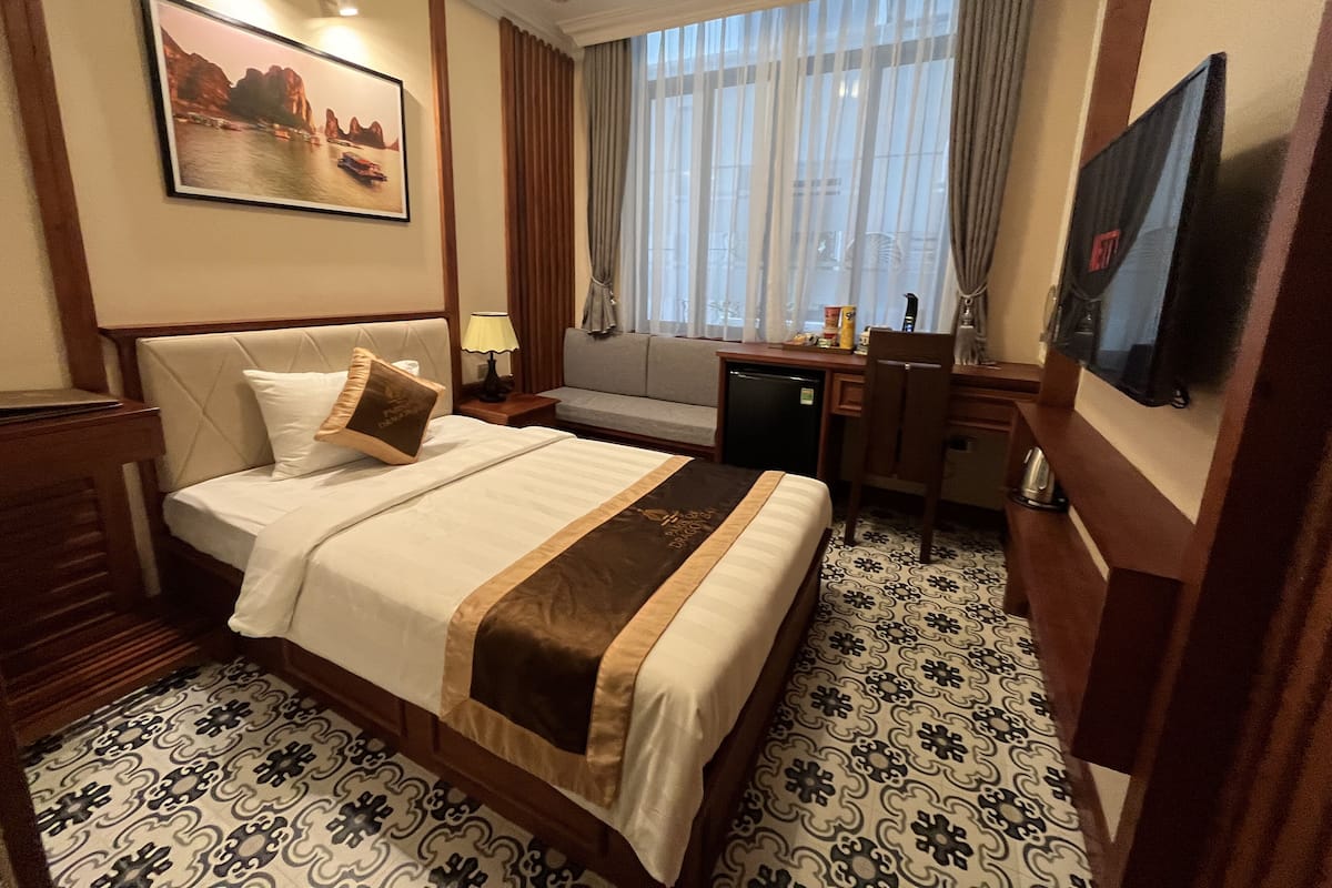 A hotel room with a bed, a desk, a chair, a TV, and a window with curtains.