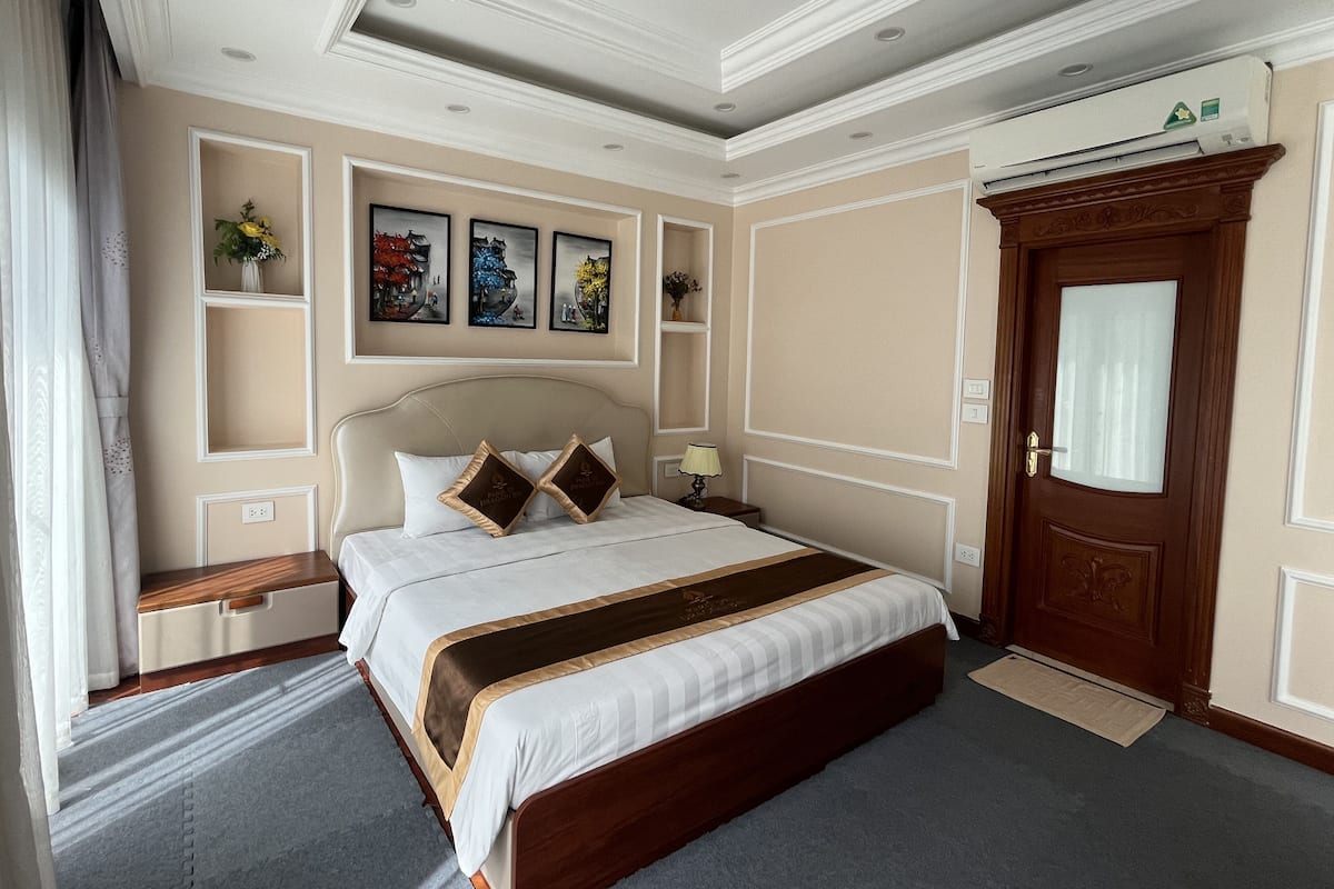 A well-appointed hotel room with a large bed, a wooden wardrobe, a desk, and a wall-mounted air conditioning unit.