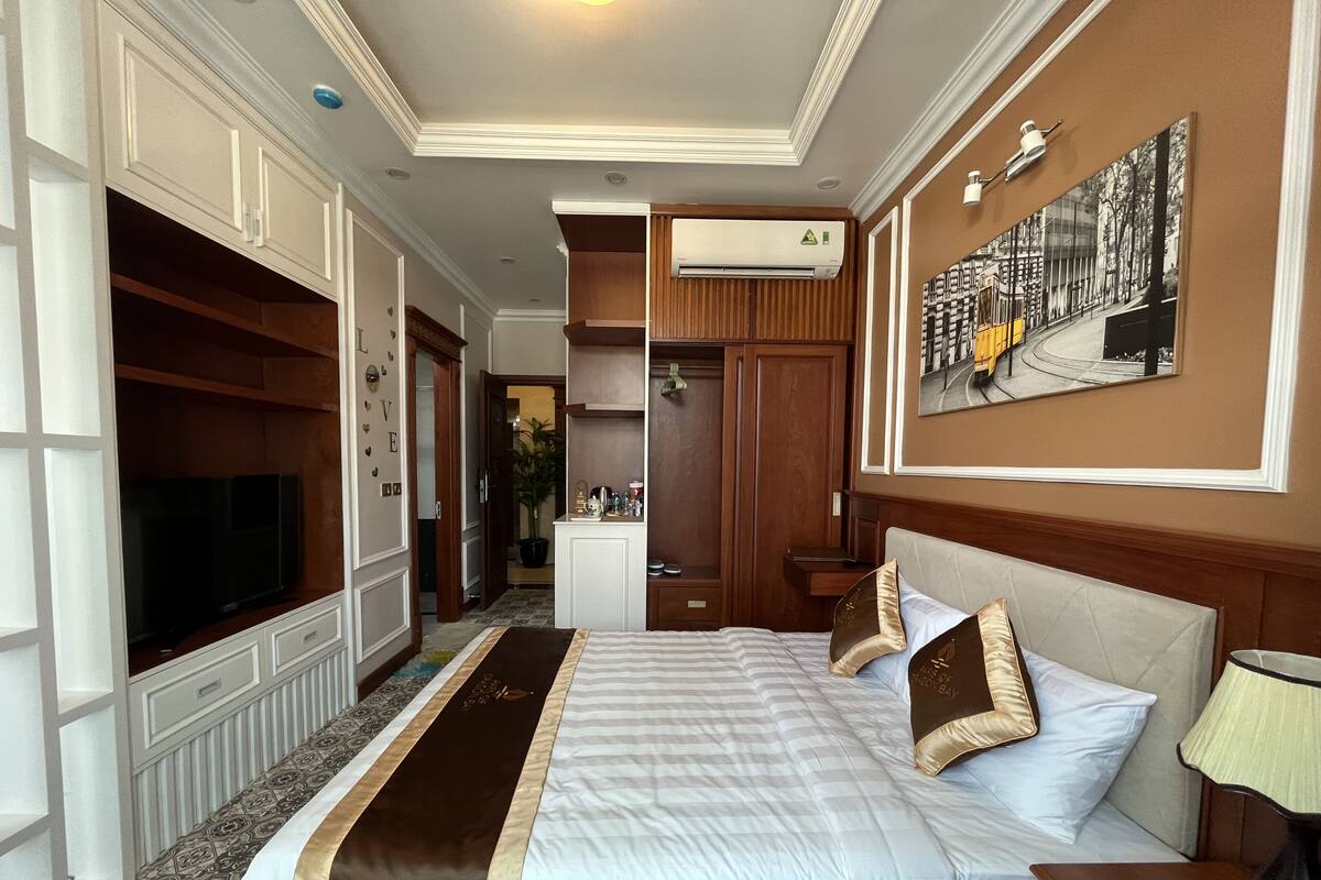 A hotel room with a large bed, a television, a desk, and a painting on the wall.