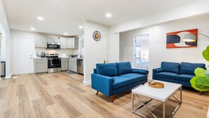 Eine moderne Wohnung mit einer Küche, zwei blauen Sofas, einem Couchtisch und einem großen Fenster.