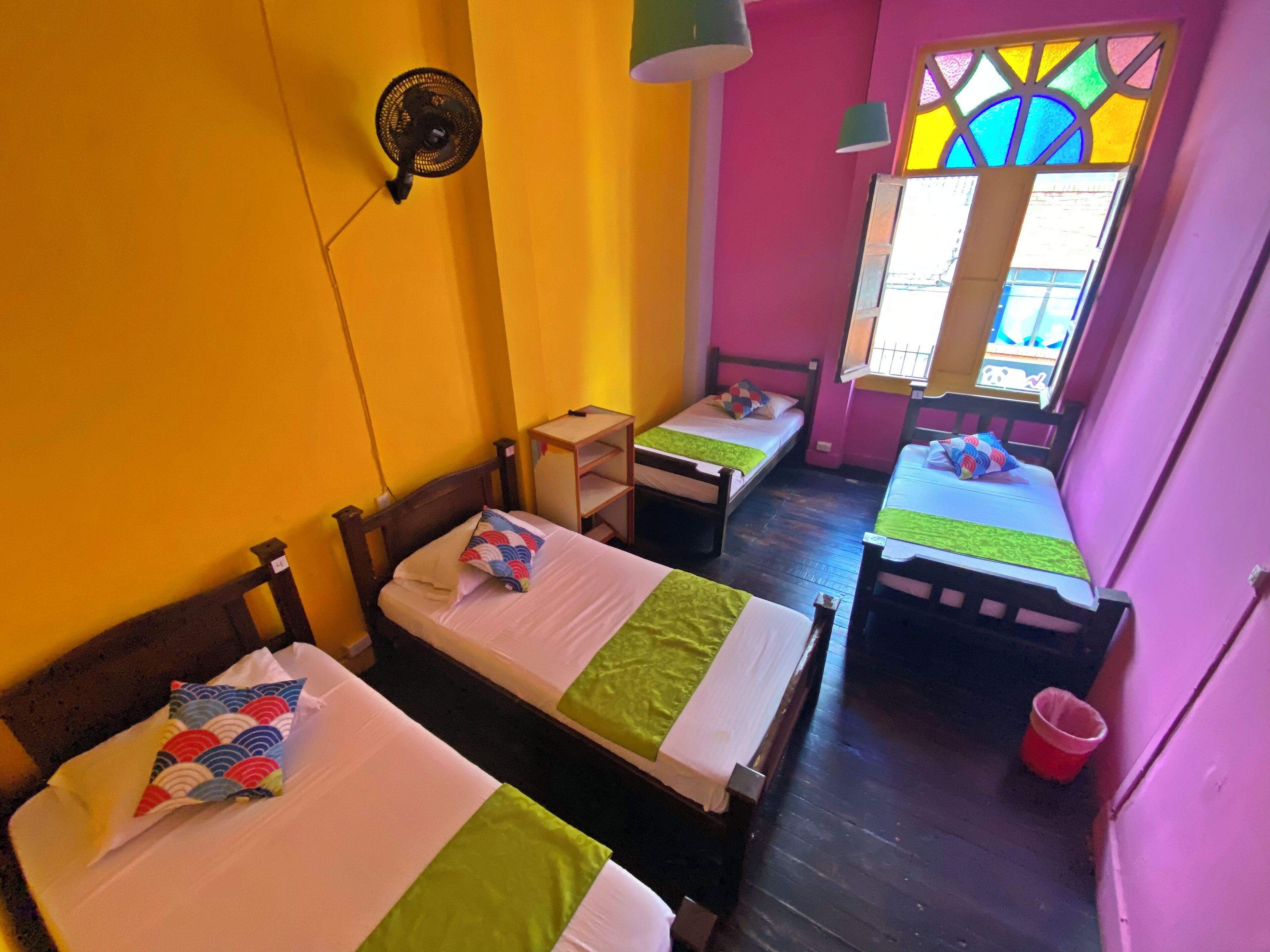 A room with two single beds, a small table, and a window with a colorful stained glass design.