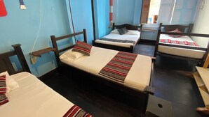 Un dormitorio con tres camas individuales, cada una con una manta y almohada a rayas. Hay un ventilador en la pared y una ventana que da a vistas del exterior.