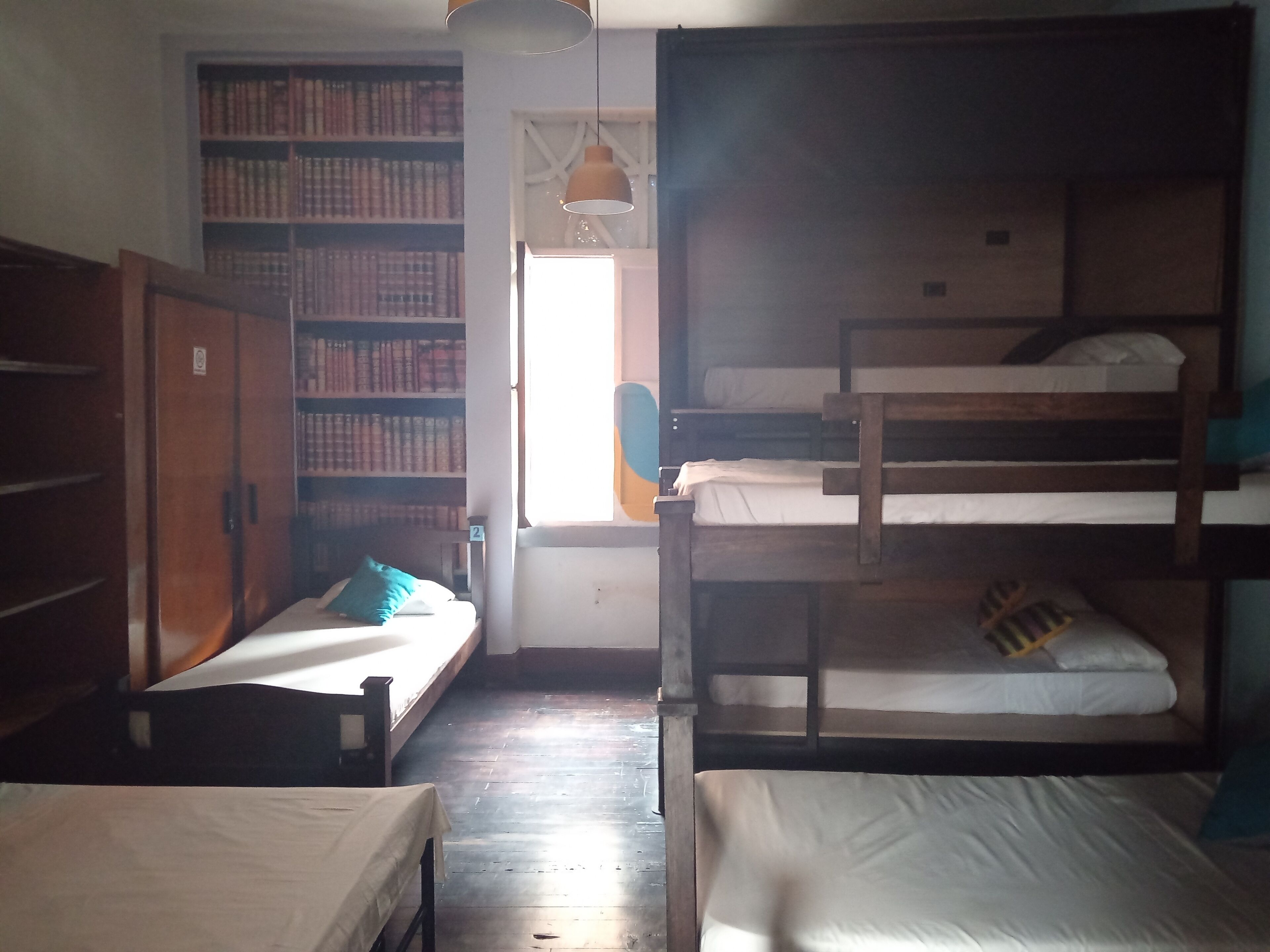A dormitory room with bunk beds, a bookshelf, and a window.