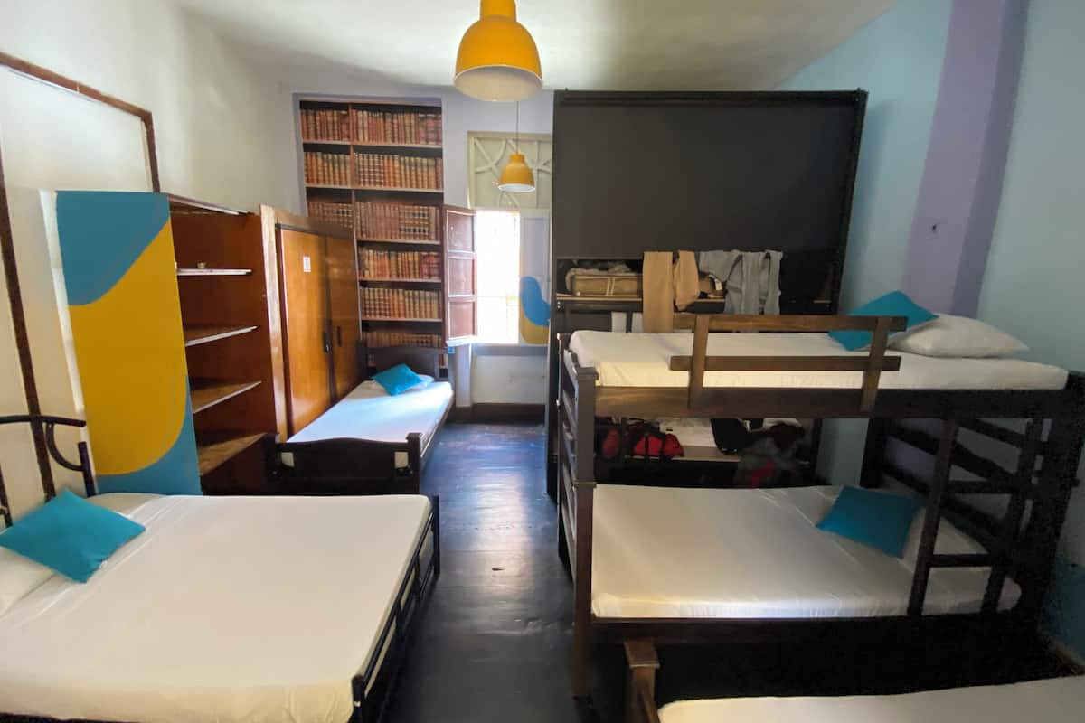 Um dormitório com beliches, uma estante de livros e uma mesa.