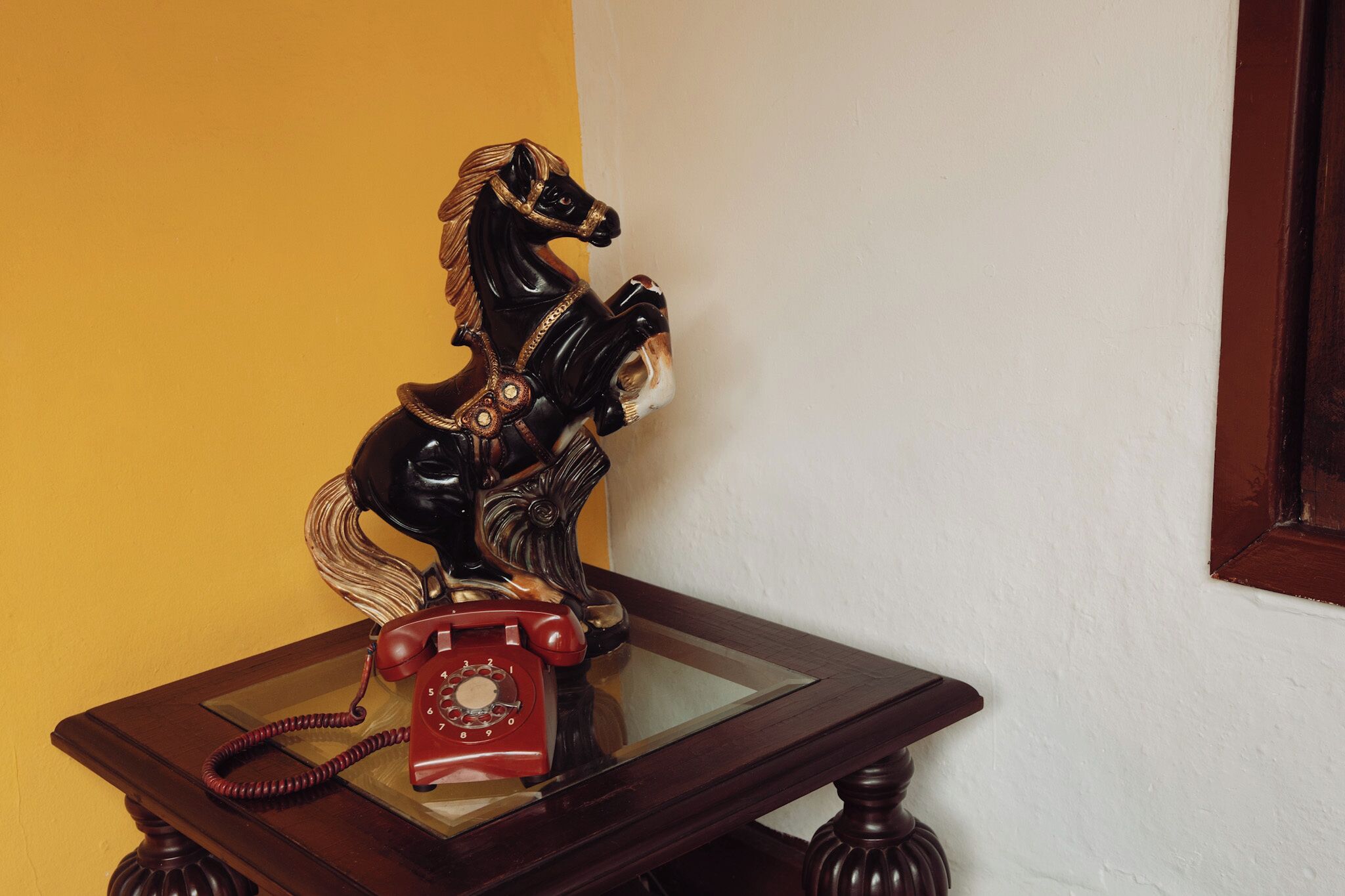 A wooden table with a rotary telephone and a decorative horse figurine.