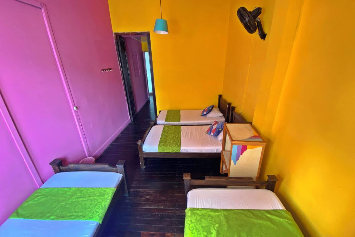 Quarto com duas camas, piso de madeira, porta rosa e parede amarela.