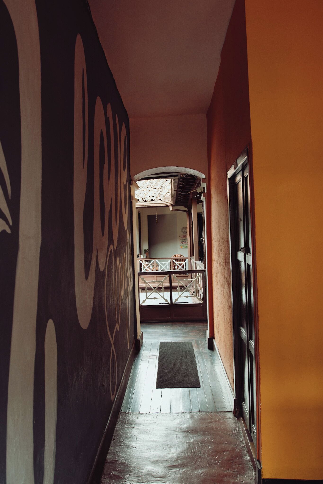 A hallway with a large wall mural, a wooden floor, and a door leading to a room with a bed and a window.