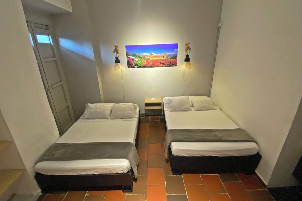 Um quarto pequeno e limpo com duas camas, um quadro na parede e uma mesinha.