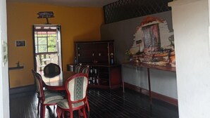 Un comedor con una mesa y sillas de madera, una ventana con vistas a follaje, y un mural en la pared.