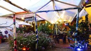 A covered outdoor area with a table and chairs, surrounded by plants and a mural on the wall.
