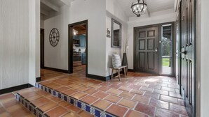 A spacious hallway with a tiled floor, a wooden bench, a clock, and a door leading to a kitchen area.