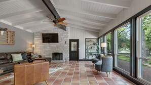 A spacious living room with a fireplace, a large window, and a ceiling fan.