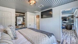 Een slaapkamer met een bed, nachtkastje en spiegel. Er is een deur die naar een andere kamer leidt.